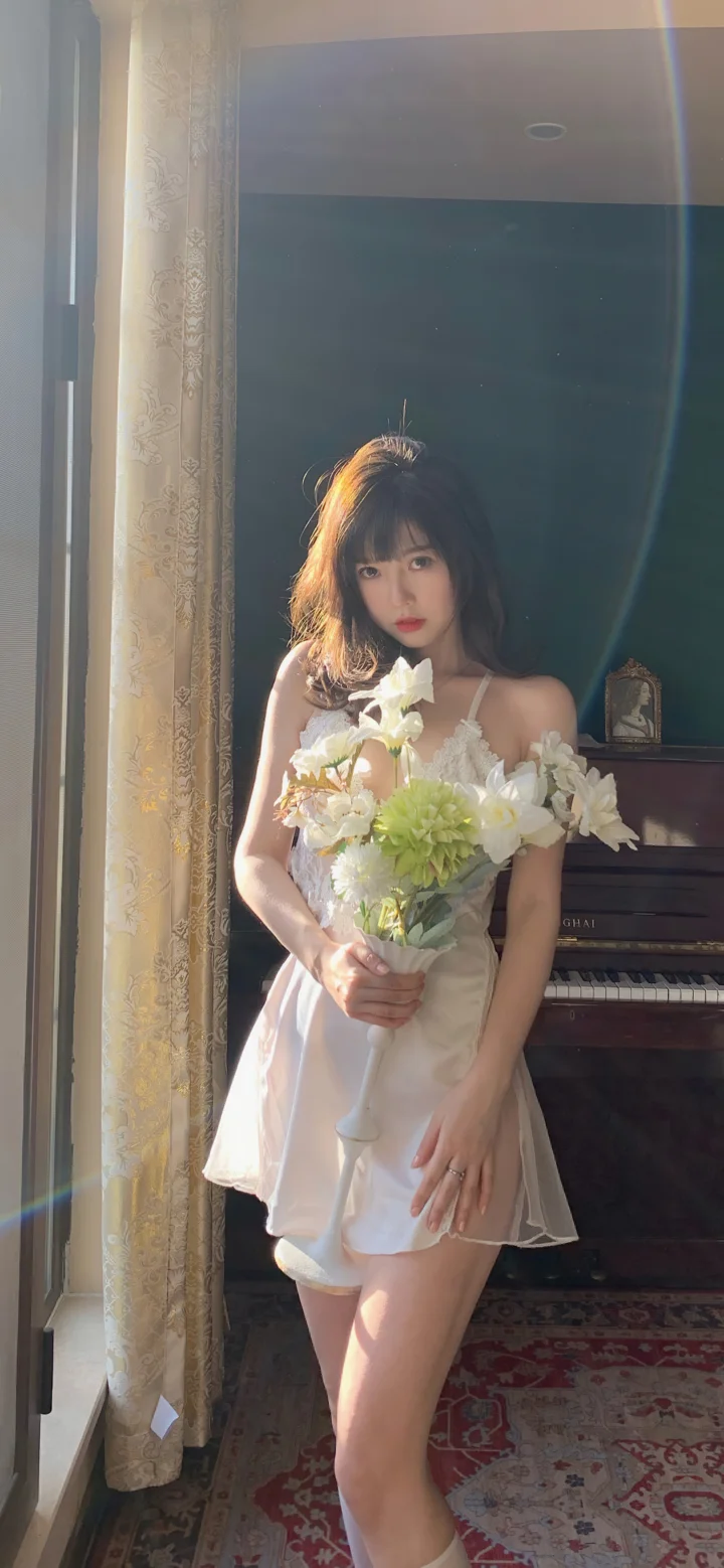 一名穿白色连衣裙的女子站在窗边，手捧花束，身后是一架钢琴。