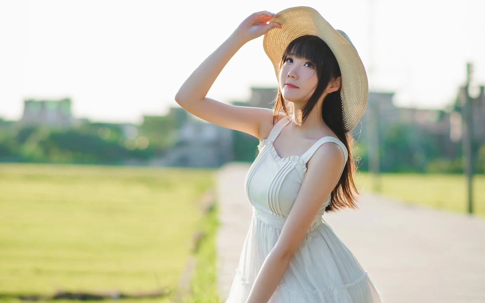 一名戴草帽、穿白色连衣裙的女性站在绿地旁的小路上。