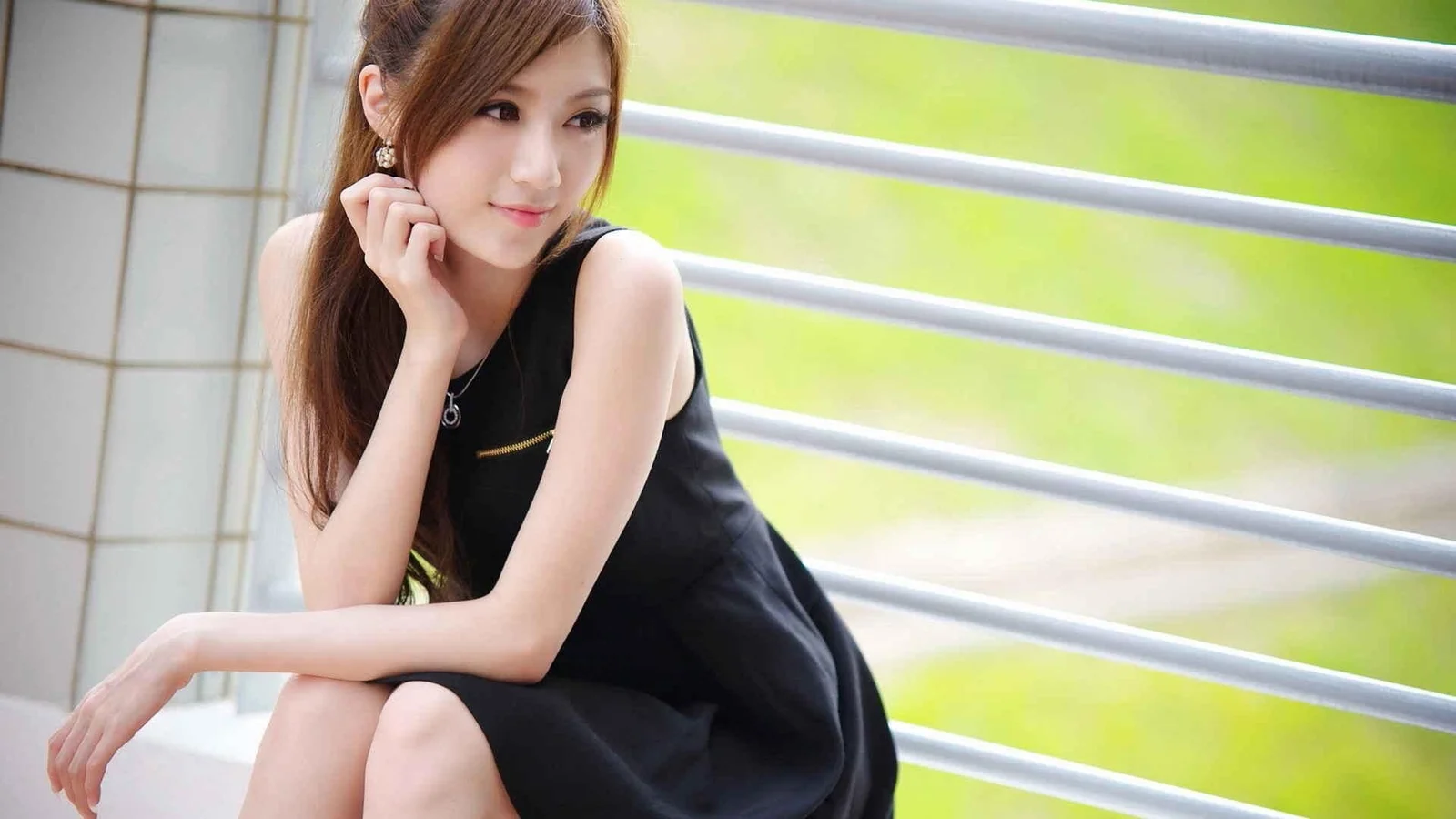一名棕色长发女性身穿黑色无袖连衣裙坐在栏杆旁。