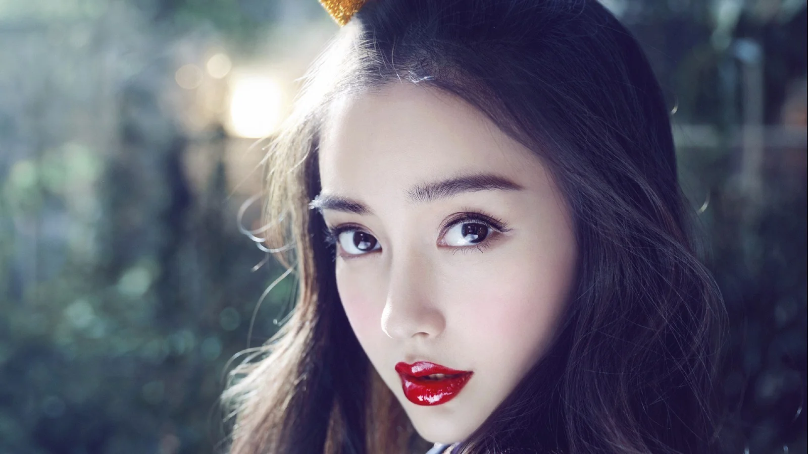 一位成年女性在柔和的森林光影中注视镜头，红唇和面部特写清晰可见。