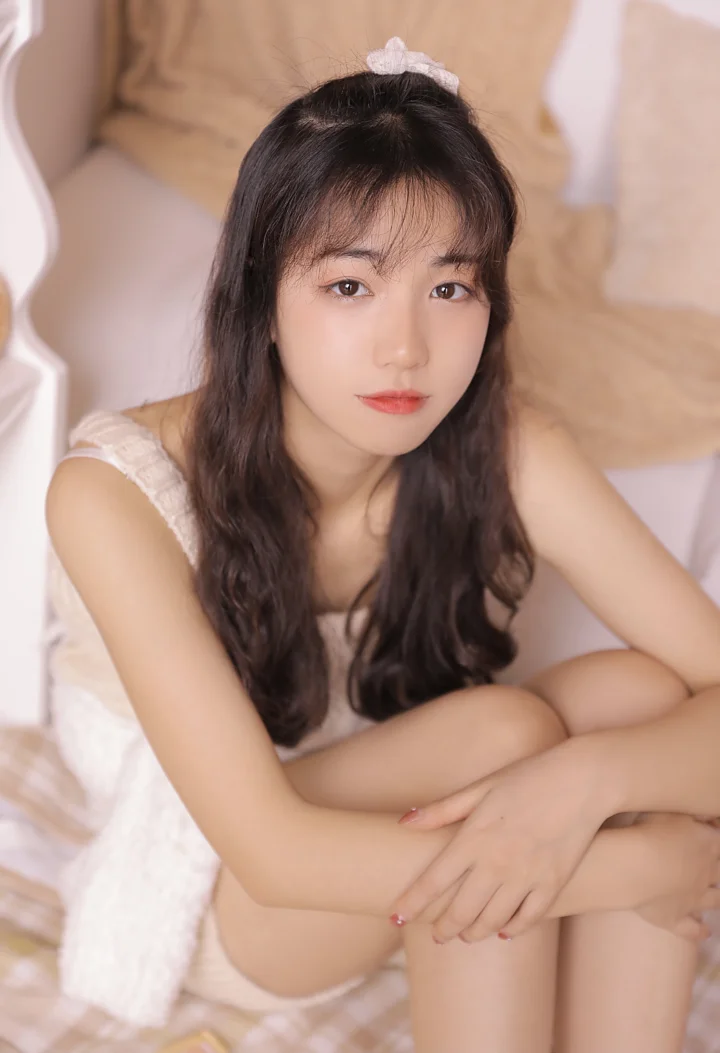 一名长发女性坐在室内柔和的浅色背景前看向镜头。