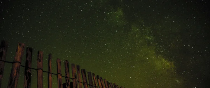 夜空中布满繁星，银河横贯画面上方，前景是一排木栅栏。