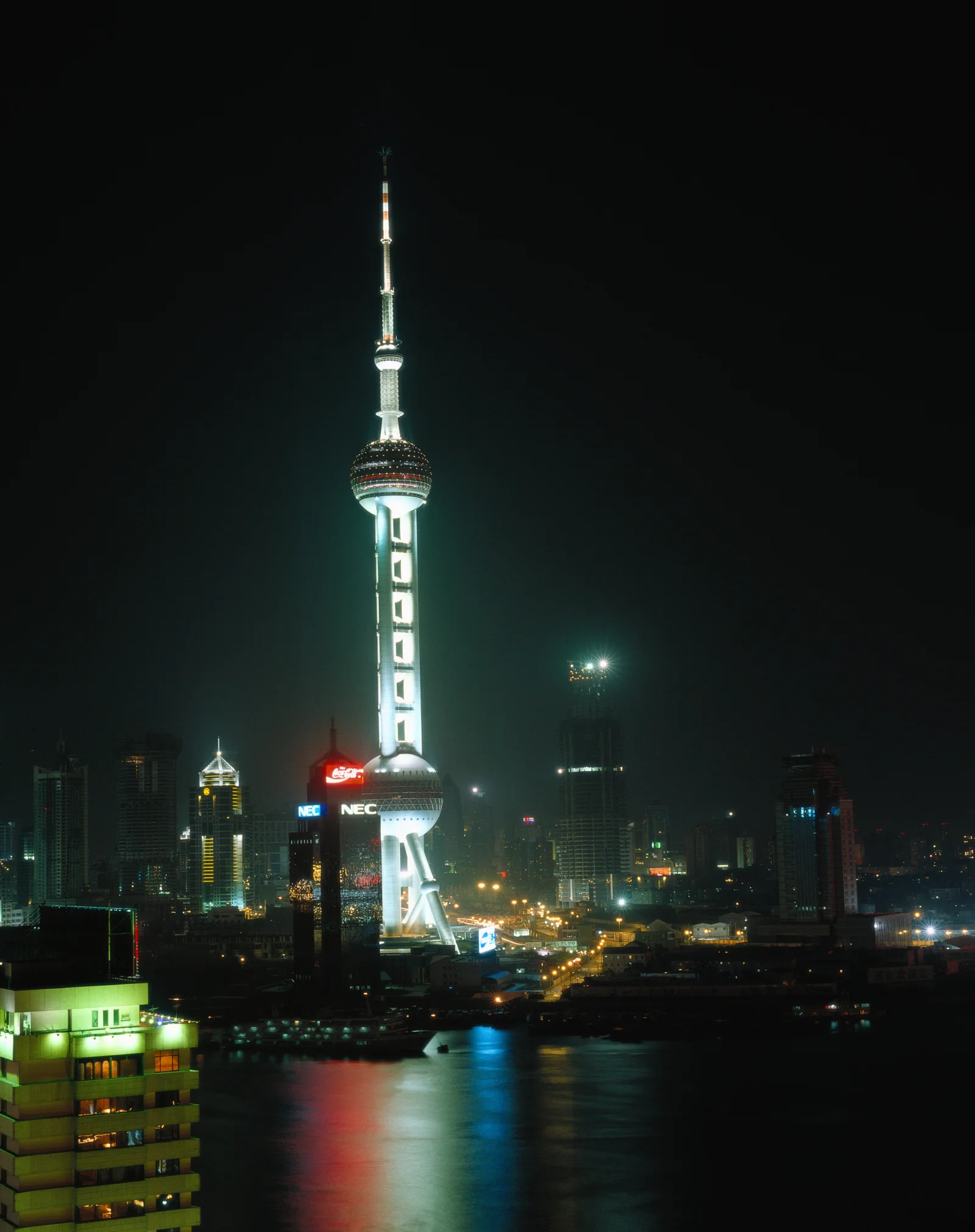夜色中的东方明珠塔矗立在城市天际线前，灯光倒映在水面上。