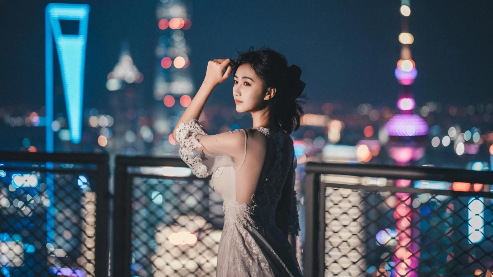 一名女子站在桥上，身后是灯光璀璨的城市夜景。
