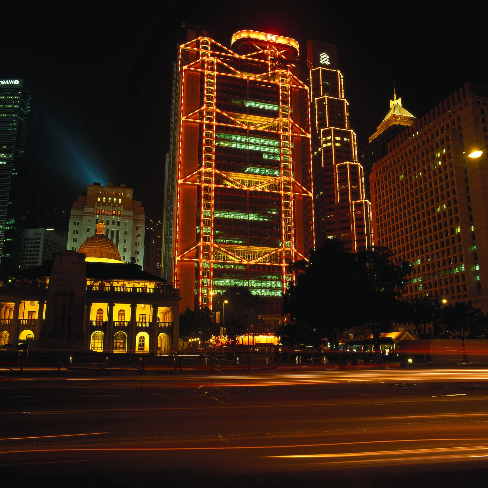 夜色中的城市高楼被橙色灯光勾勒，前景道路上留下明亮的车流光轨。