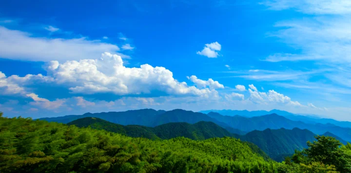 蓝天下层叠的群山、茂密森林与白云构成开阔的自然风景。