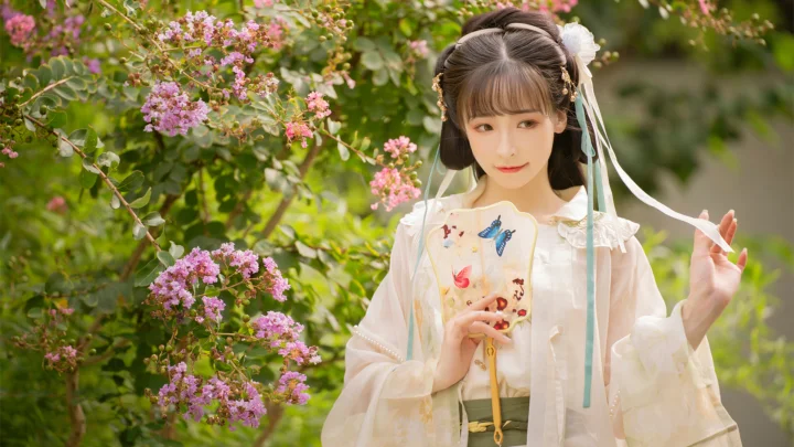 一名身穿浅色服装的女子站在盛开着粉色花朵的绿意花园中。