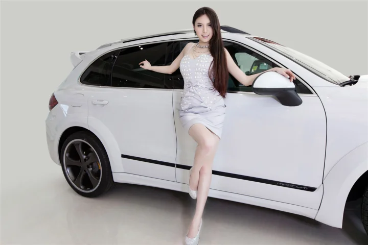 一名女性站在白色汽车旁，置身于简洁的室内背景中。