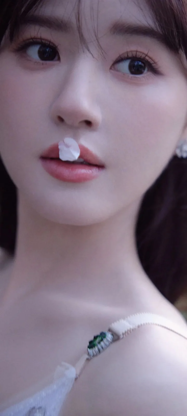 一名女性的面部与肩部特写，嘴唇附近可见一小片白色花瓣。