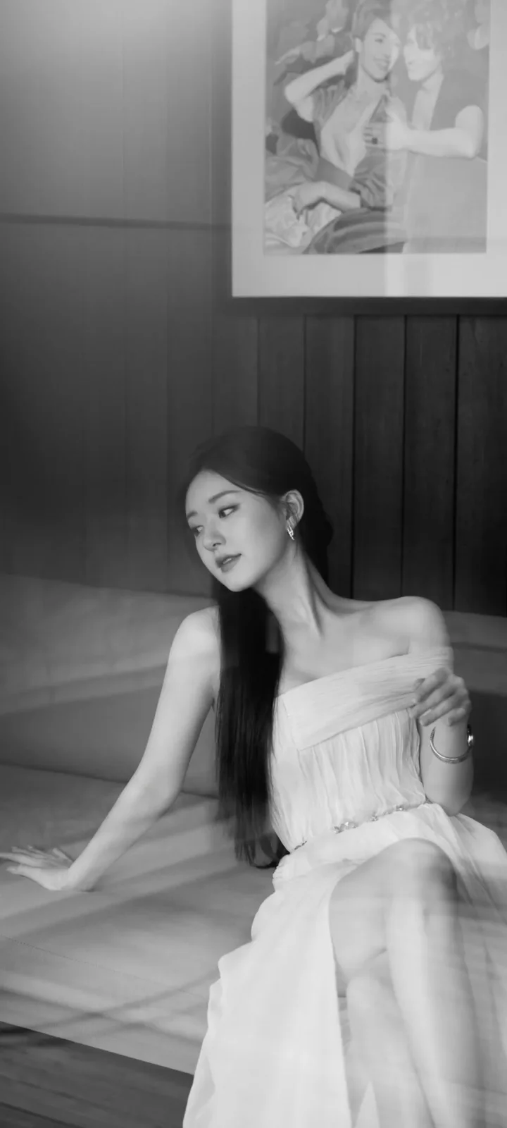 一位身穿白色连衣裙的女性坐在室内沙发上，画面呈黑白色调。