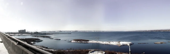 画面展现了冬日海湾、覆雪小岛、远处建筑和前景桥梁。
