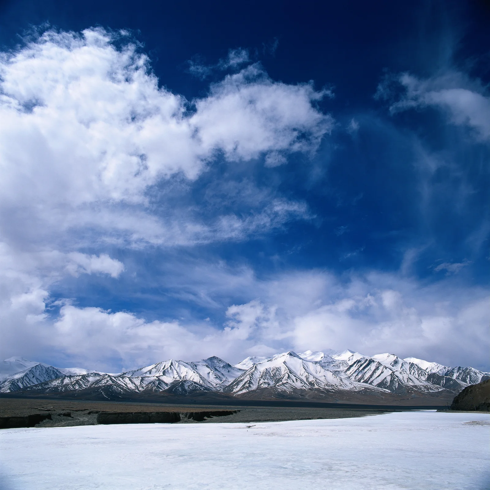蓝天下的积云映衬着远处的雪山，前景是一片冰雪覆盖的平原。