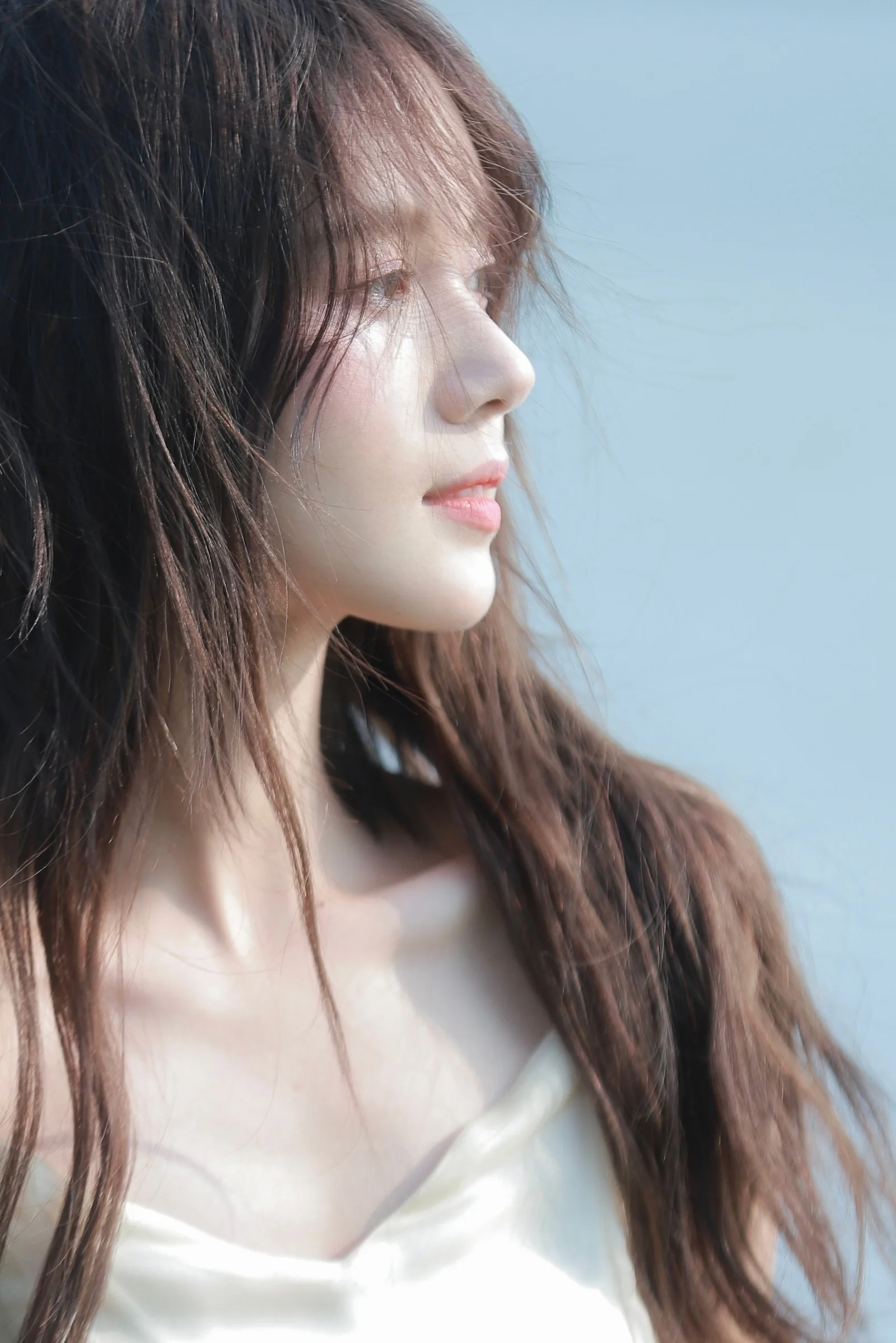 一名长发女性面向右侧，以侧脸姿态出现在浅蓝色背景前。