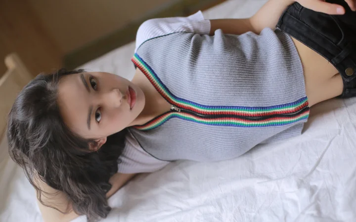 一名女性躺在白色床单上，身穿灰色针织上衣和深色短裤。