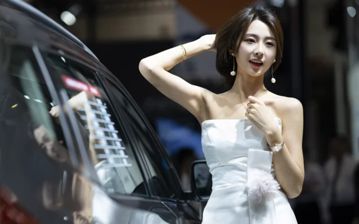 흰색 드레스를 입은 성인 여성이 자동차 옆에서 머리를 정리하고 있다.