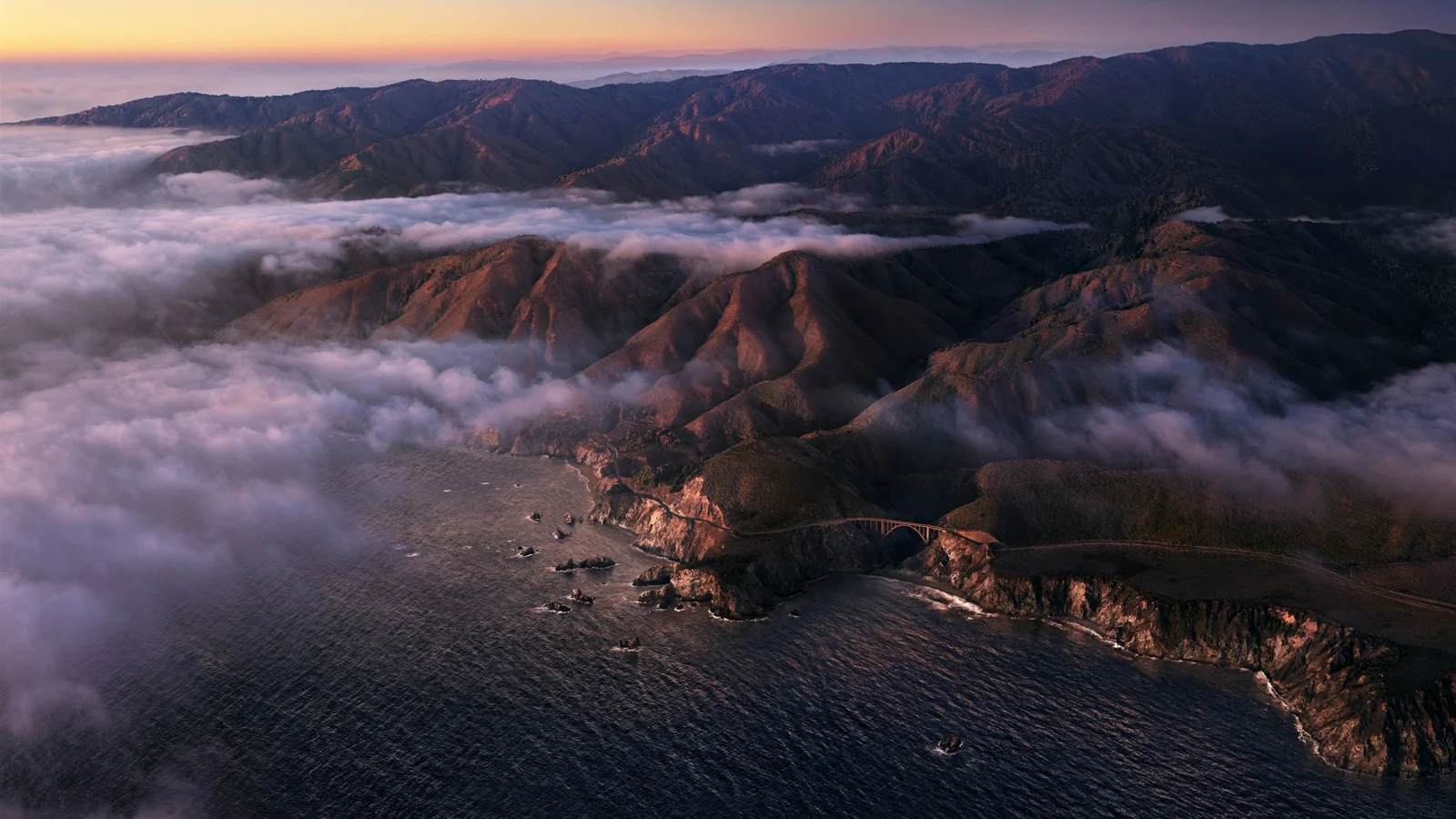 暮色映照下的山脉、海岸与云海构成壮阔的航拍风景。