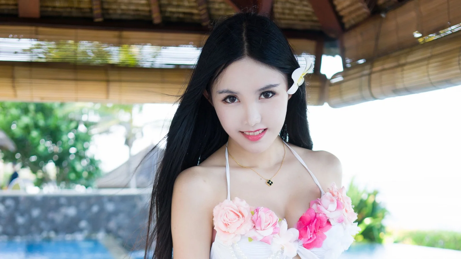 一名长发女子在竹帘和花朵背景前微笑看向镜头。