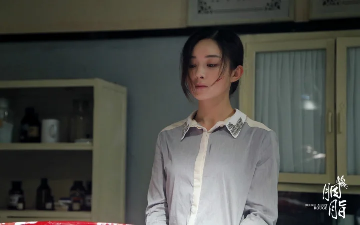 一名穿白衬衫的女性站在室内，背景可见柜子、瓶罐和窗户。
