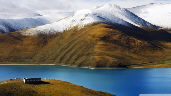 积雪覆盖的山脉环绕着宁静的蓝色湖泊，前景是一座小型建筑。