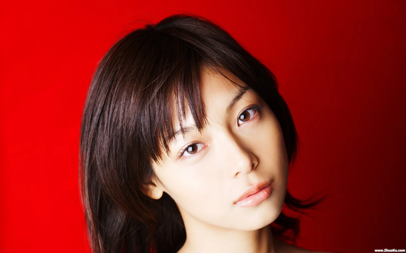 鮮やかな赤い背景の前に成人女性のクローズアップポートレートが写っている。