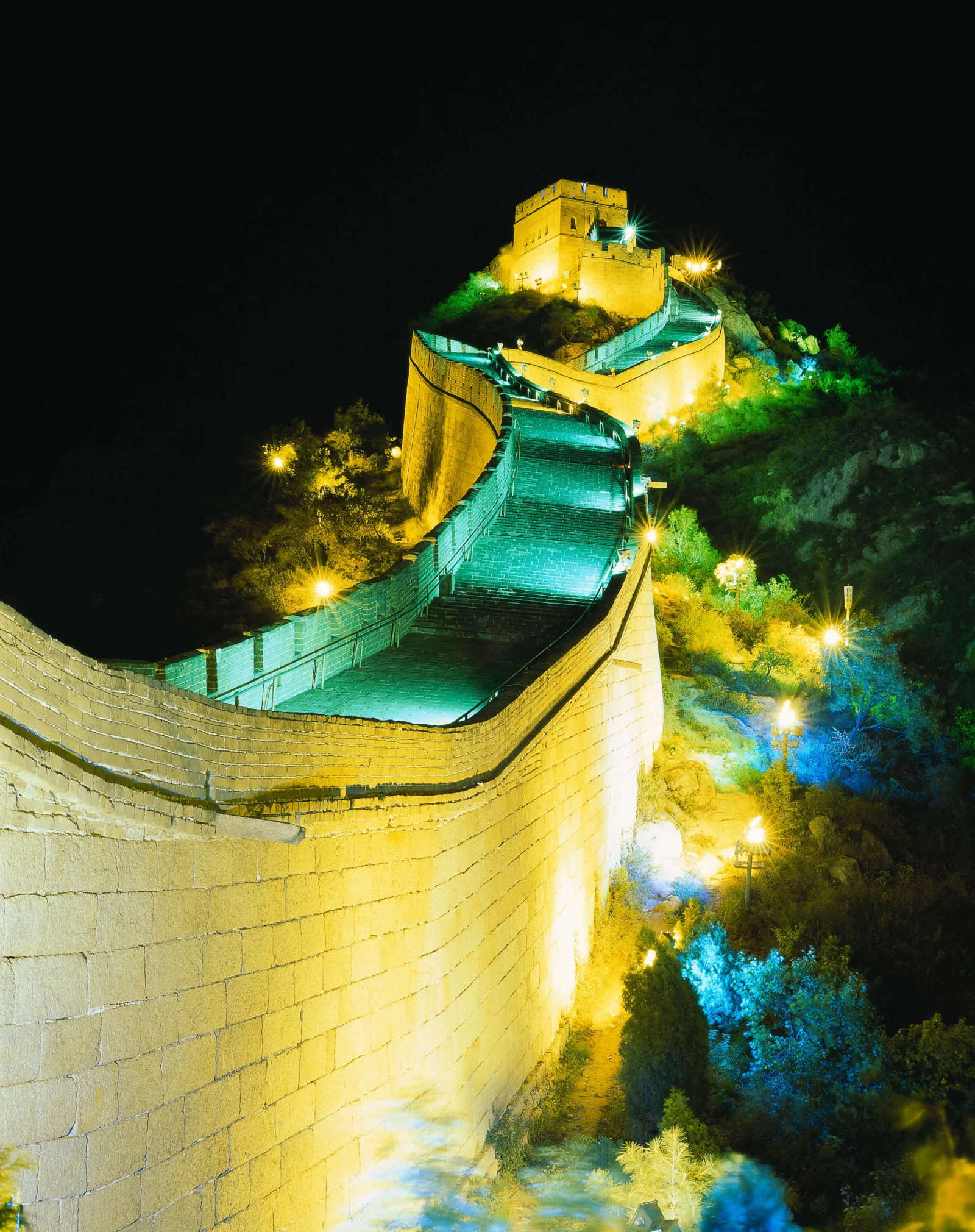 夜晚灯光照亮蜿蜒的长城城墙与山顶烽火台，周围被黑色夜空环绕。