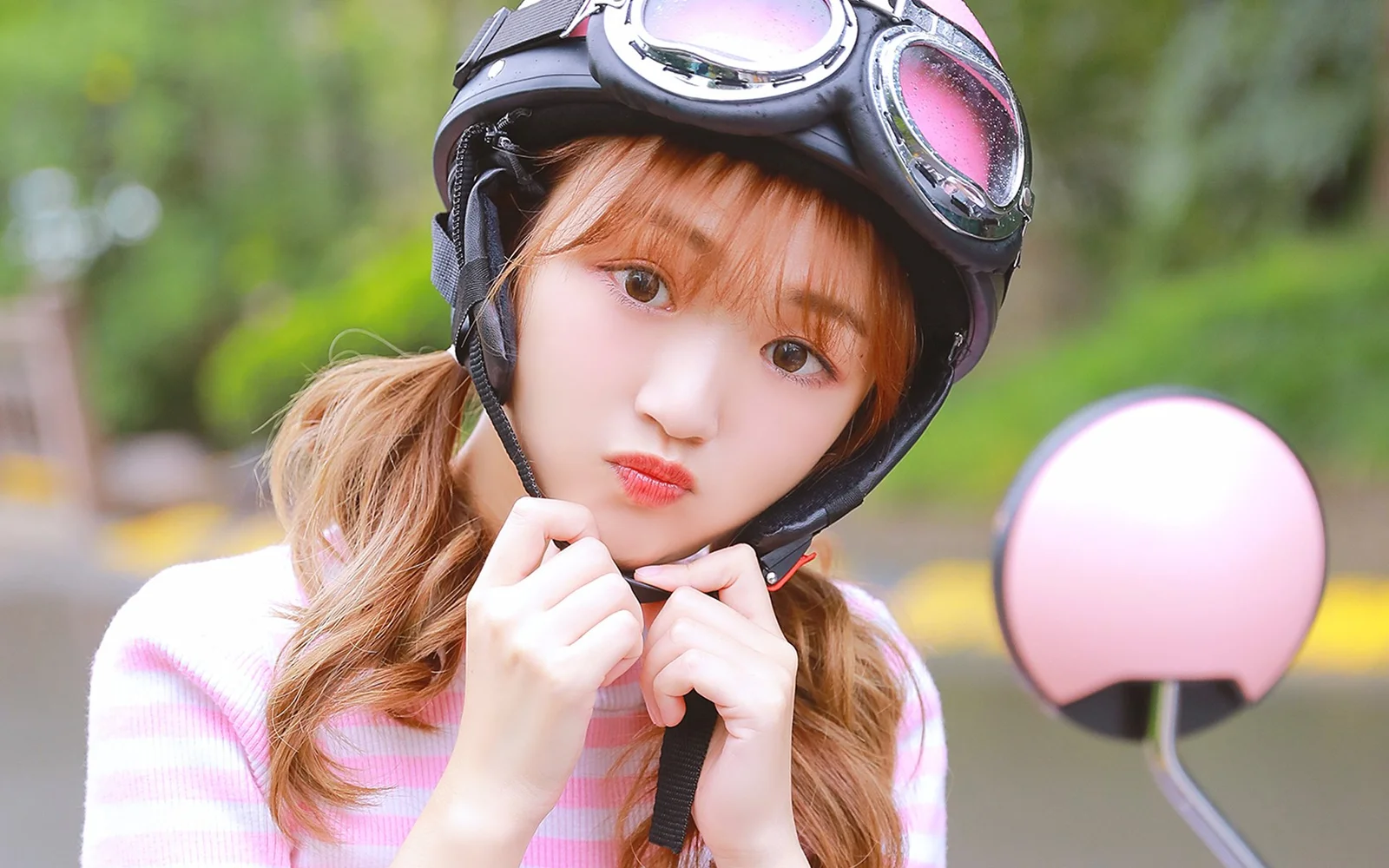 검은 헬멧과 고글을 쓴 여성이 야외에서 턱끈을 정리하고 있다.