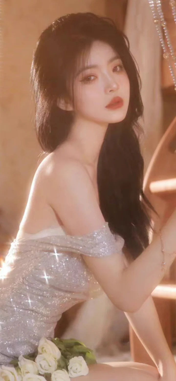 一名长发女性身穿银色亮片礼服，在暖色光线下侧身面对镜头。