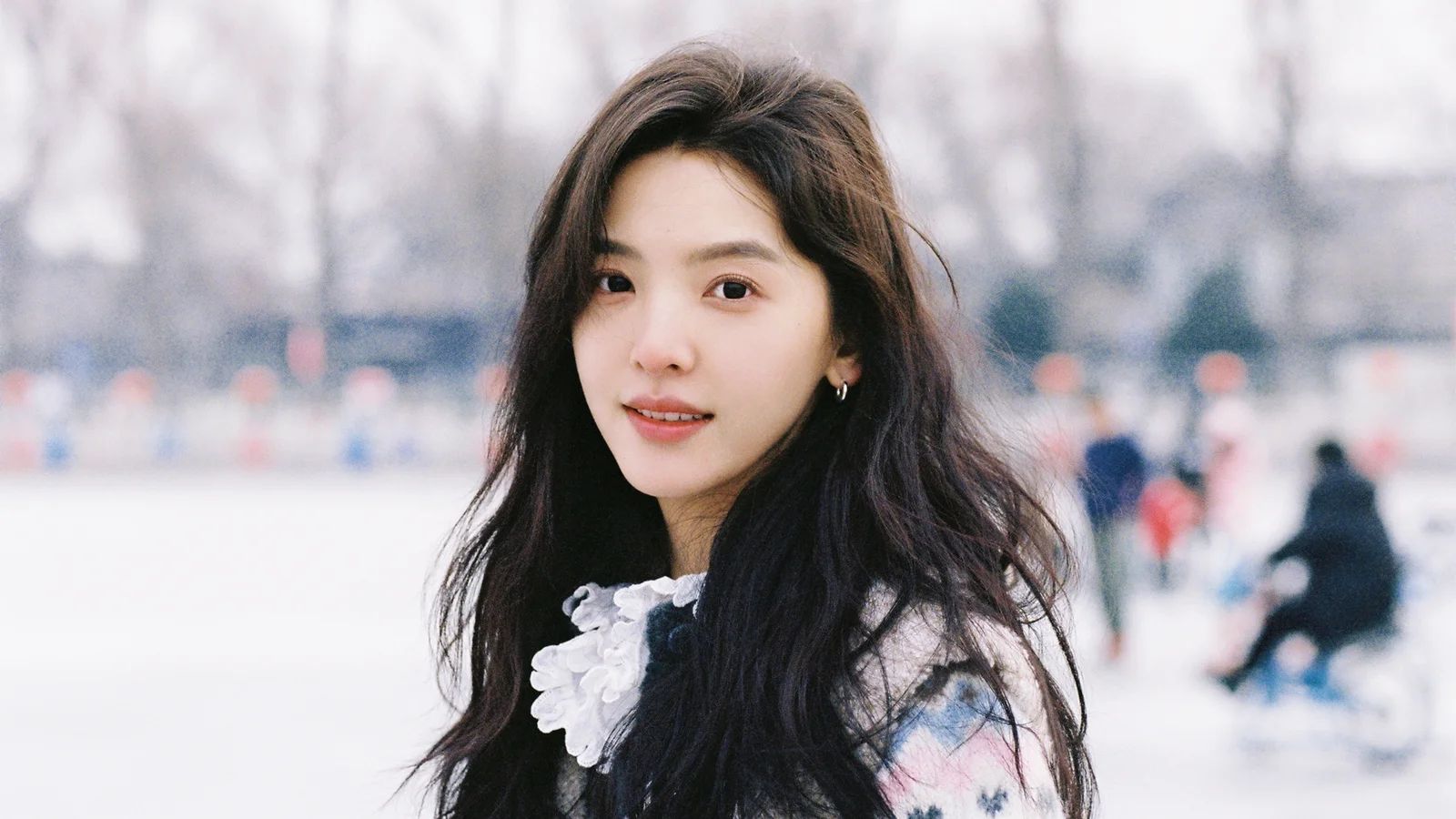 一名长发女性在户外背景前面向镜头微笑。