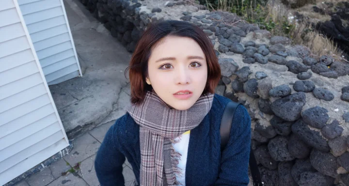 一名成年女性戴着格纹围巾站在石墙旁的户外人像画面。