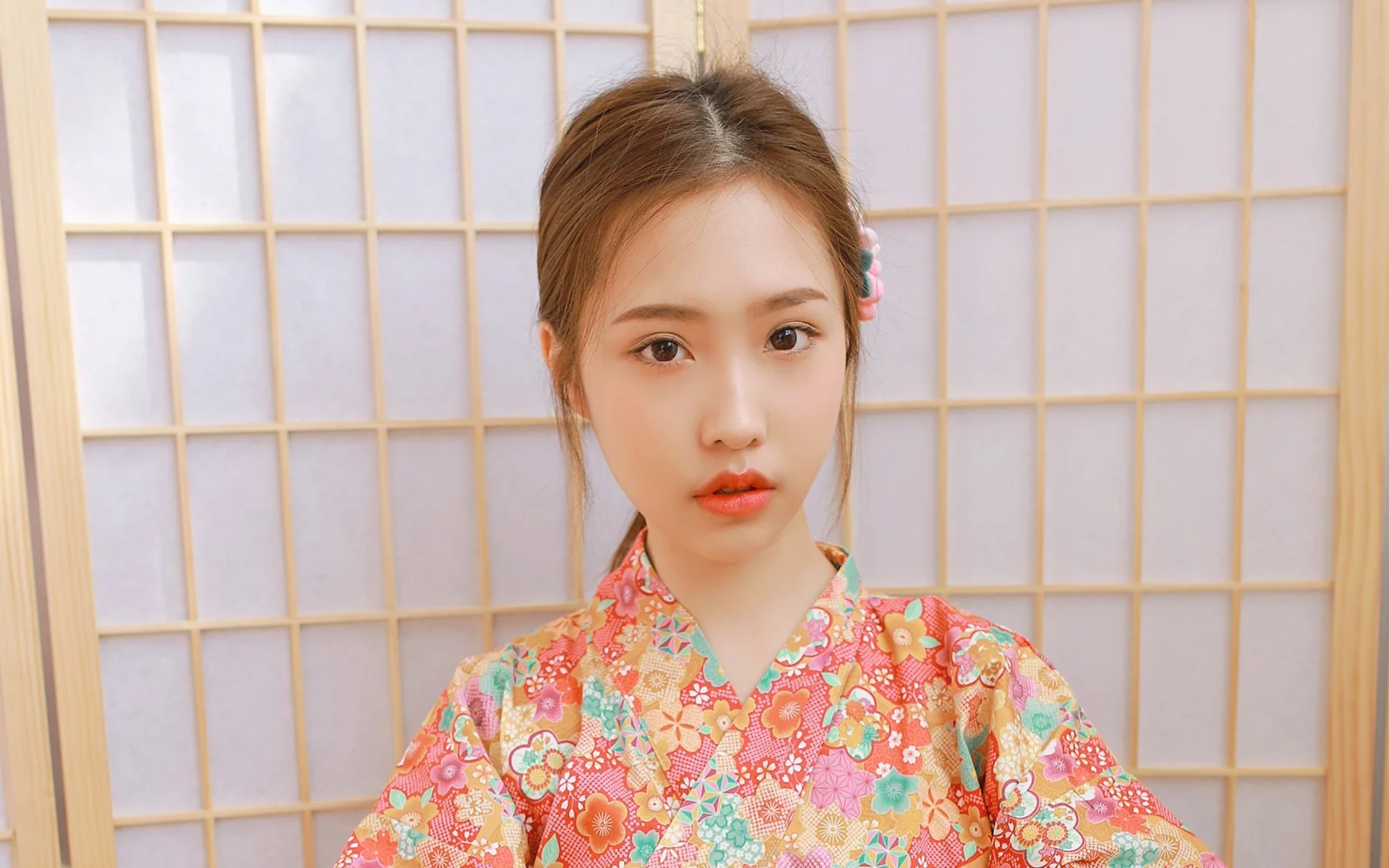 一位成年女性身穿彩色花纹服饰，在格栅屏风前面对镜头。