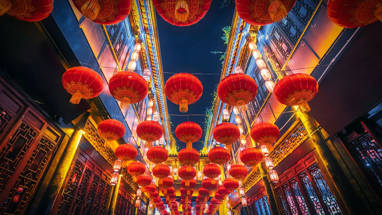 夜晚的传统街道上悬挂着成排红灯笼，两侧建筑被暖色灯光照亮。