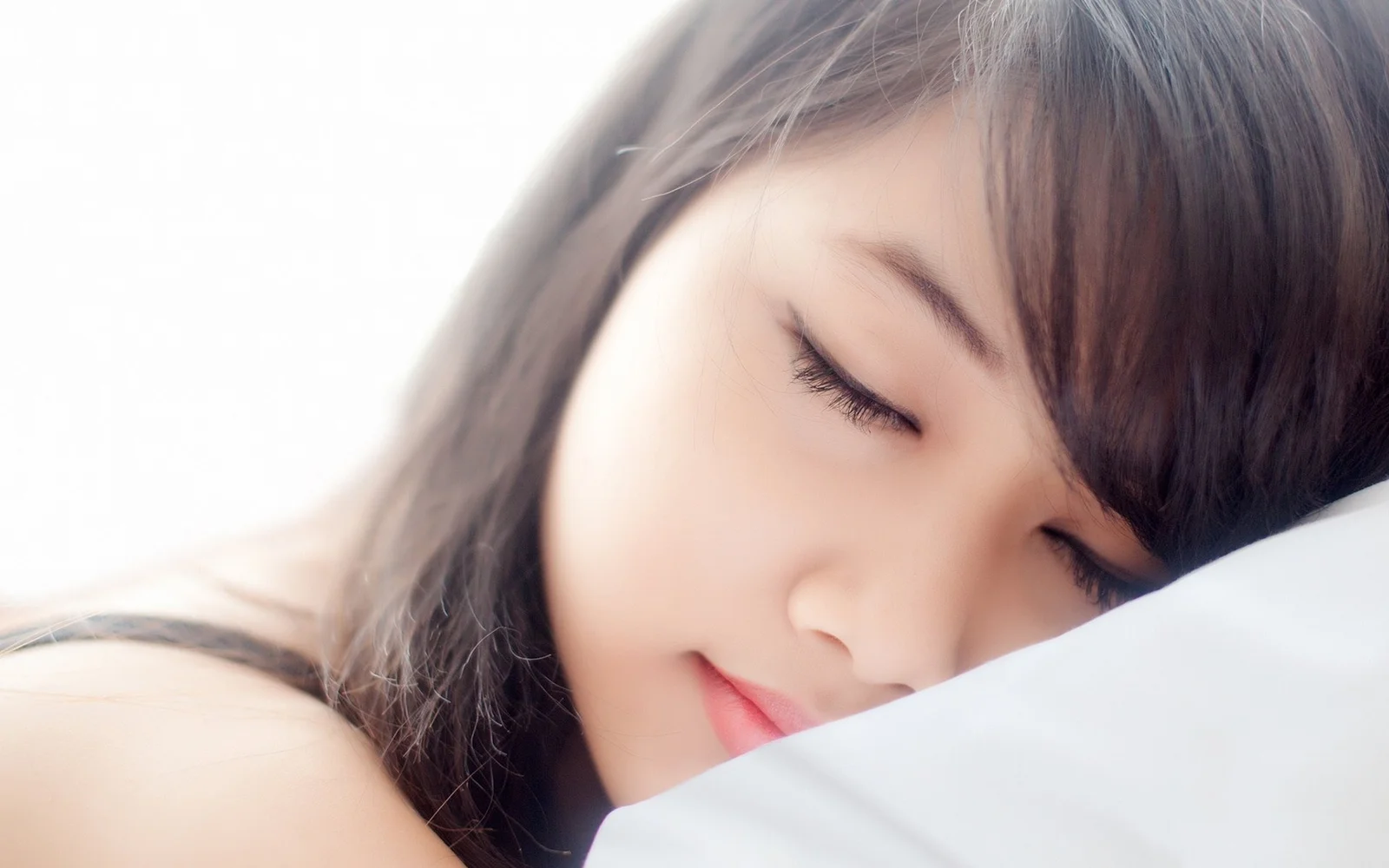 一名成年女性闭着眼睛侧靠在白色枕头上熟睡。