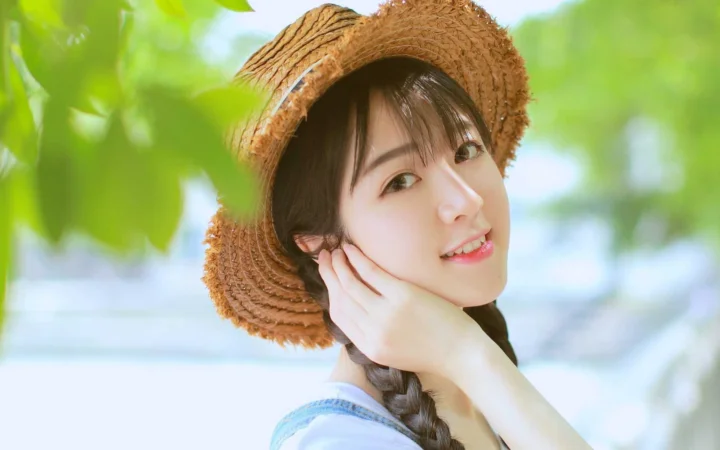 一位戴着草帽、编着辫子的女性在绿叶映衬下微笑。