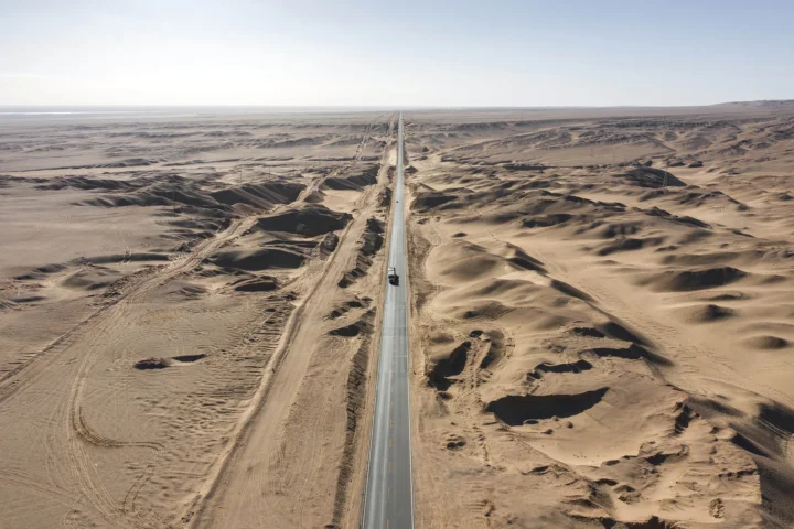 一条笔直的公路穿过广阔的荒漠沙丘，延伸至远方地平线。