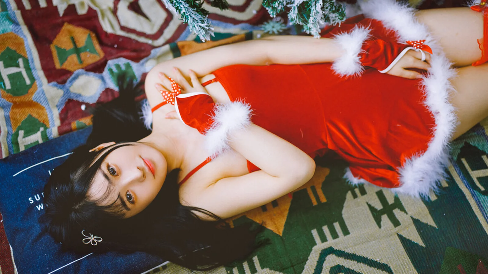 一名成年女性身穿红色圣诞风连衣裙，躺在彩色图案地毯上。