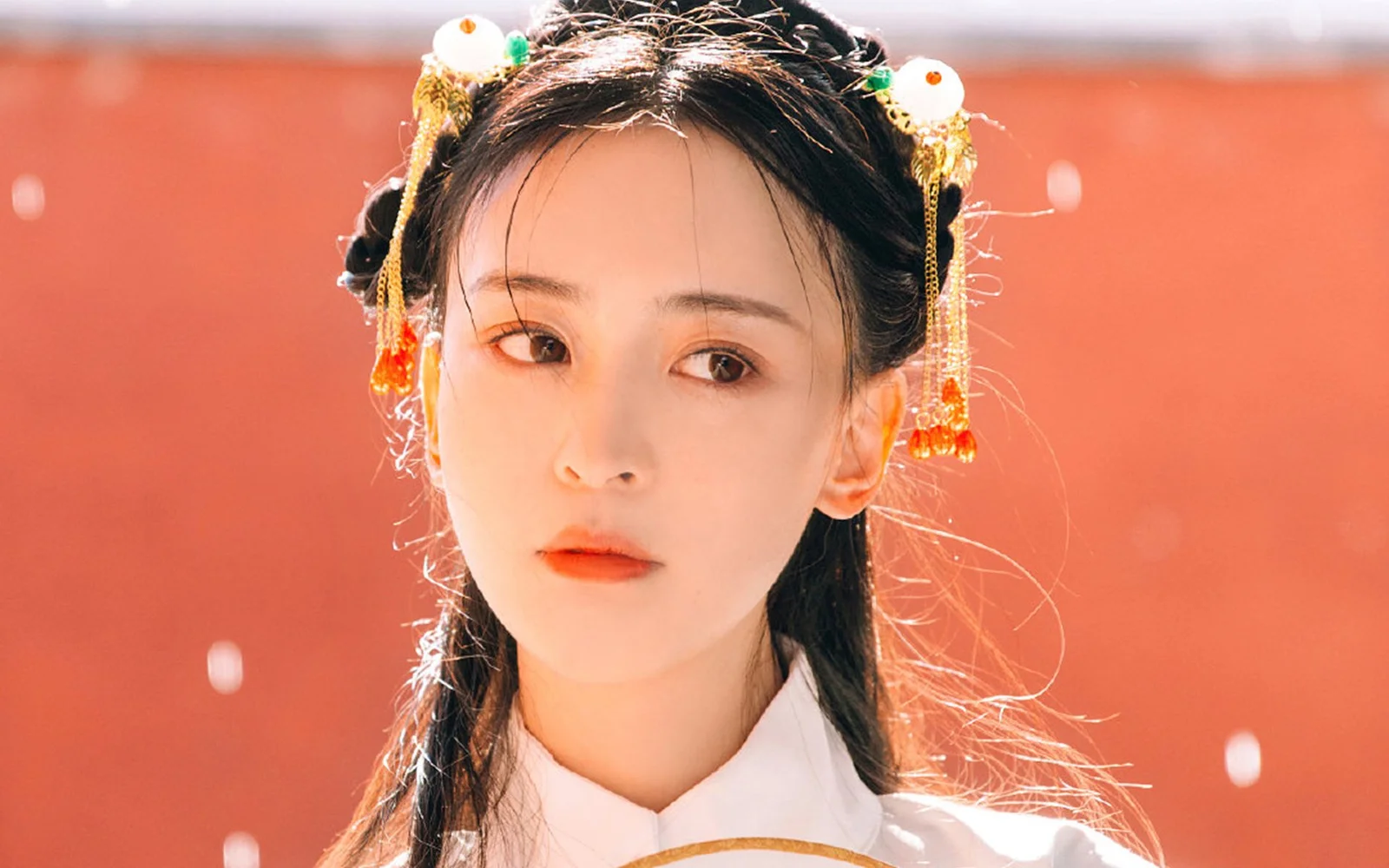 흰색 의상과 전통 머리 장식을 한 성인 여성이 붉은 배경 앞에 있는 클로즈업 초상입니다.
