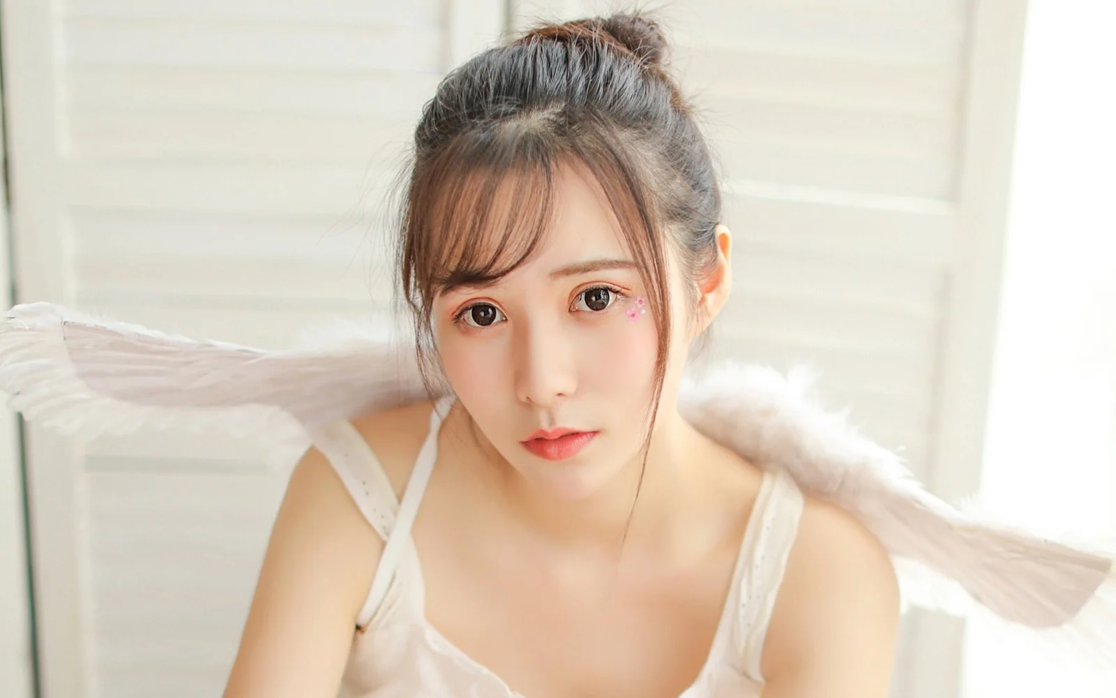 흰색 캐미솔을 입은 여성이 카메라를 바라보고 있으며 뒤에 흰색 깃털 장식이 보인다.