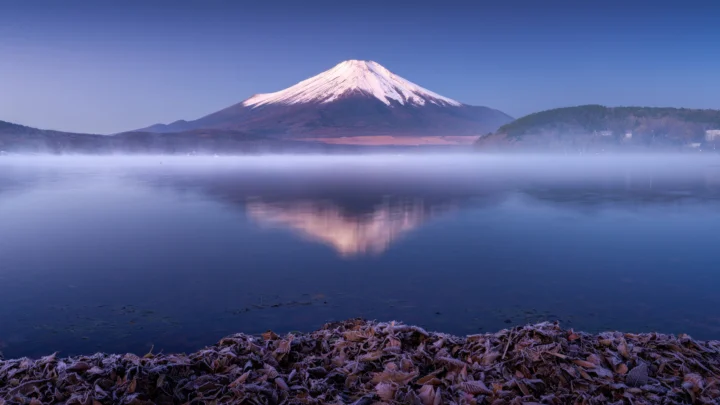雪を頂いた山が、朝霧に包まれた静かな湖面に映っている。