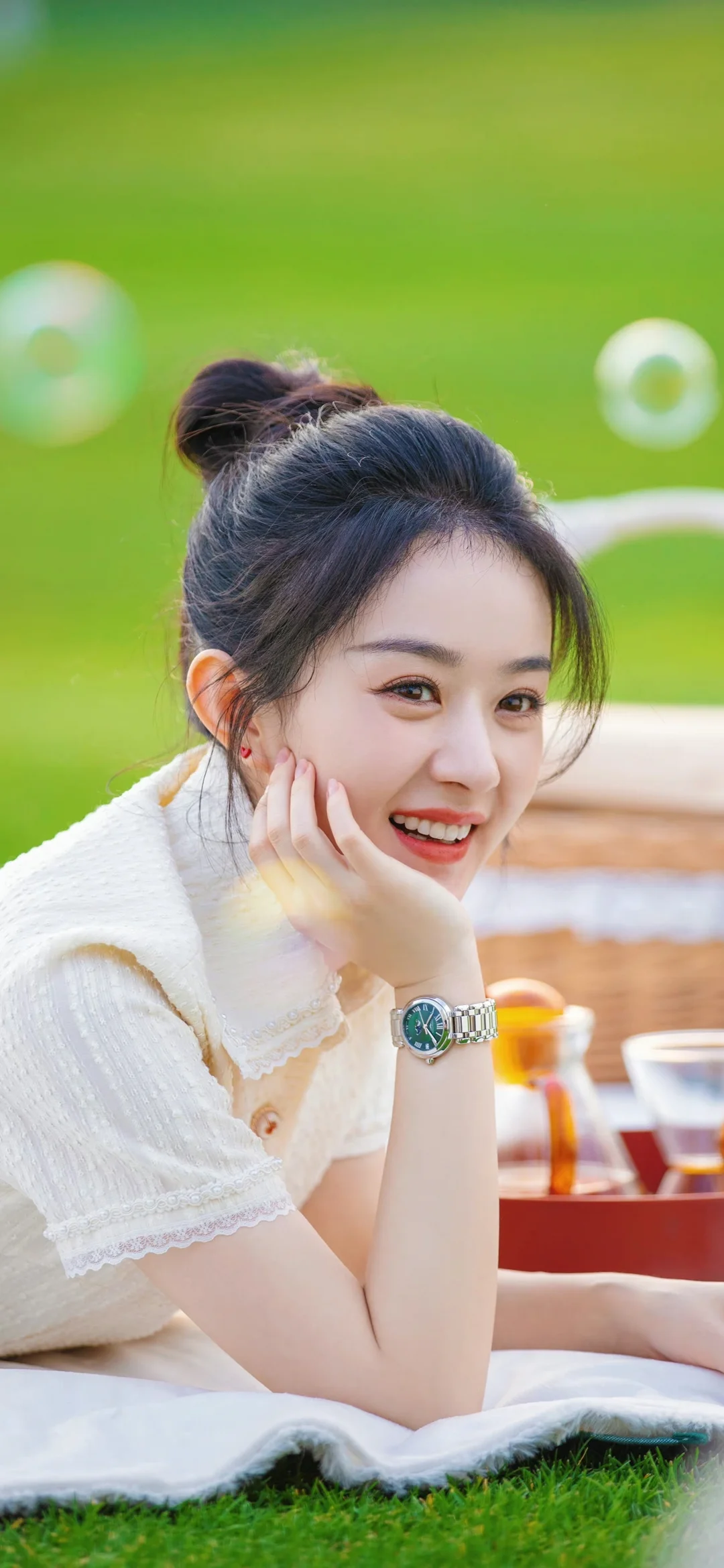 푸른 잔디 위에서 손으로 뺨을 괴고 카메라를 향해 미소 짓는 성인 여성이다.