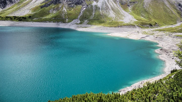 碧 turquoise 的高山湖泊映照着陡峭山坡，前景覆盖着绿色灌木。