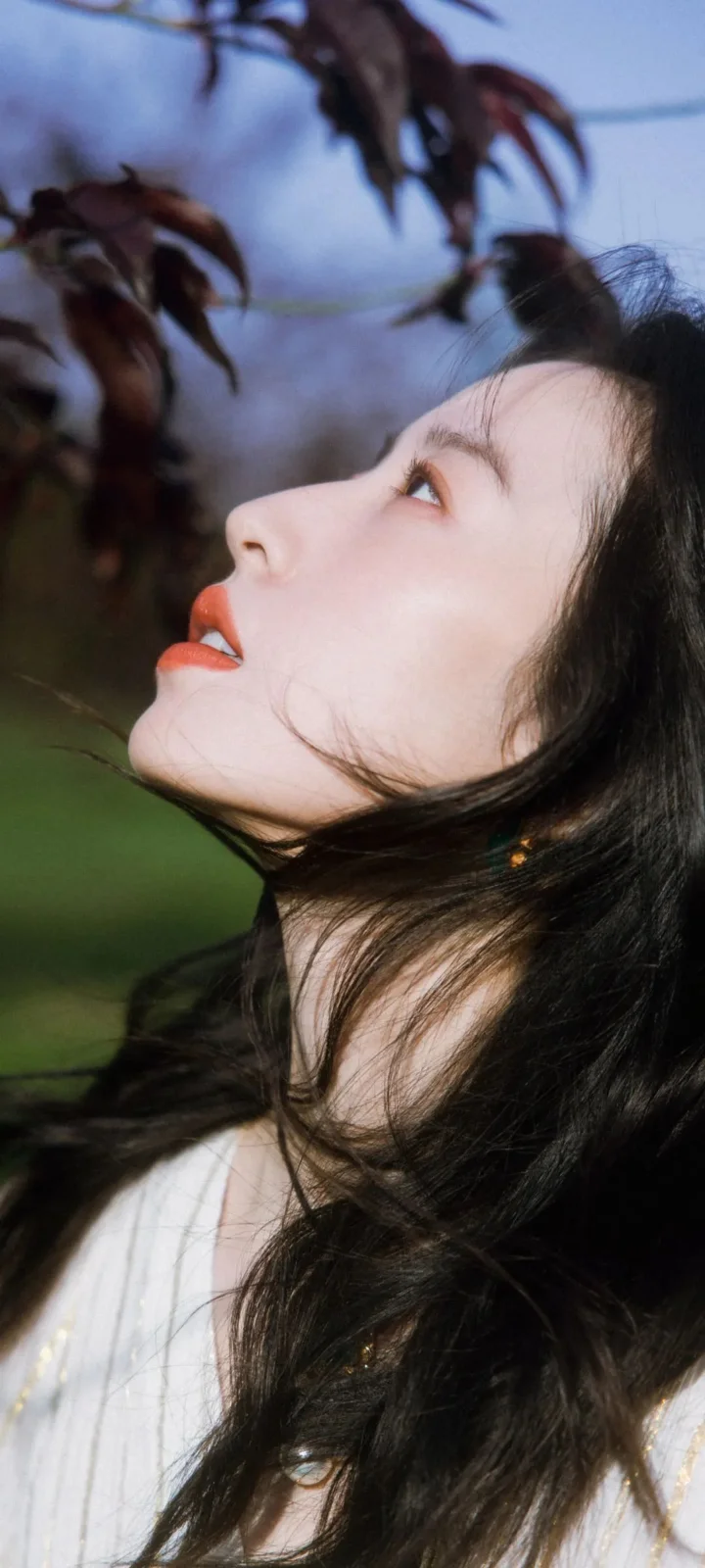 一位长发女性在户外树叶背景前仰望的侧脸肖像。