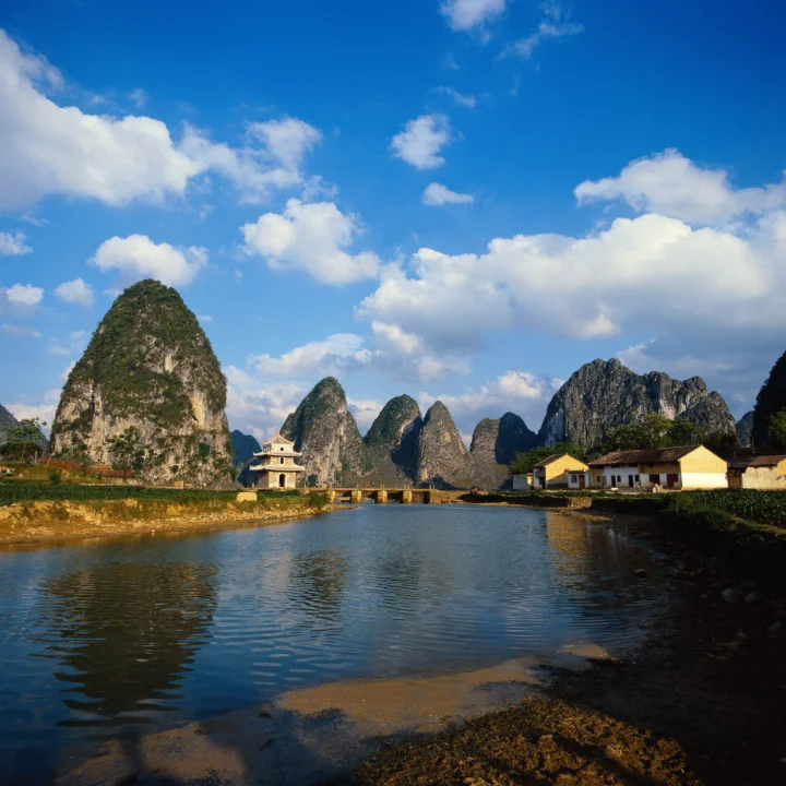 蓝天白云下，群山环绕着宁静的河流与岸边建筑。
