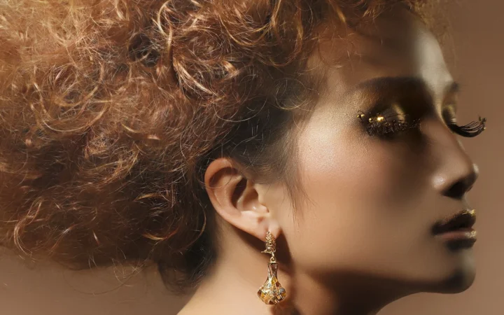 画面展示一位成年女性的卷发侧面肖像，她佩戴金色耳坠并带有装饰性眼妆。