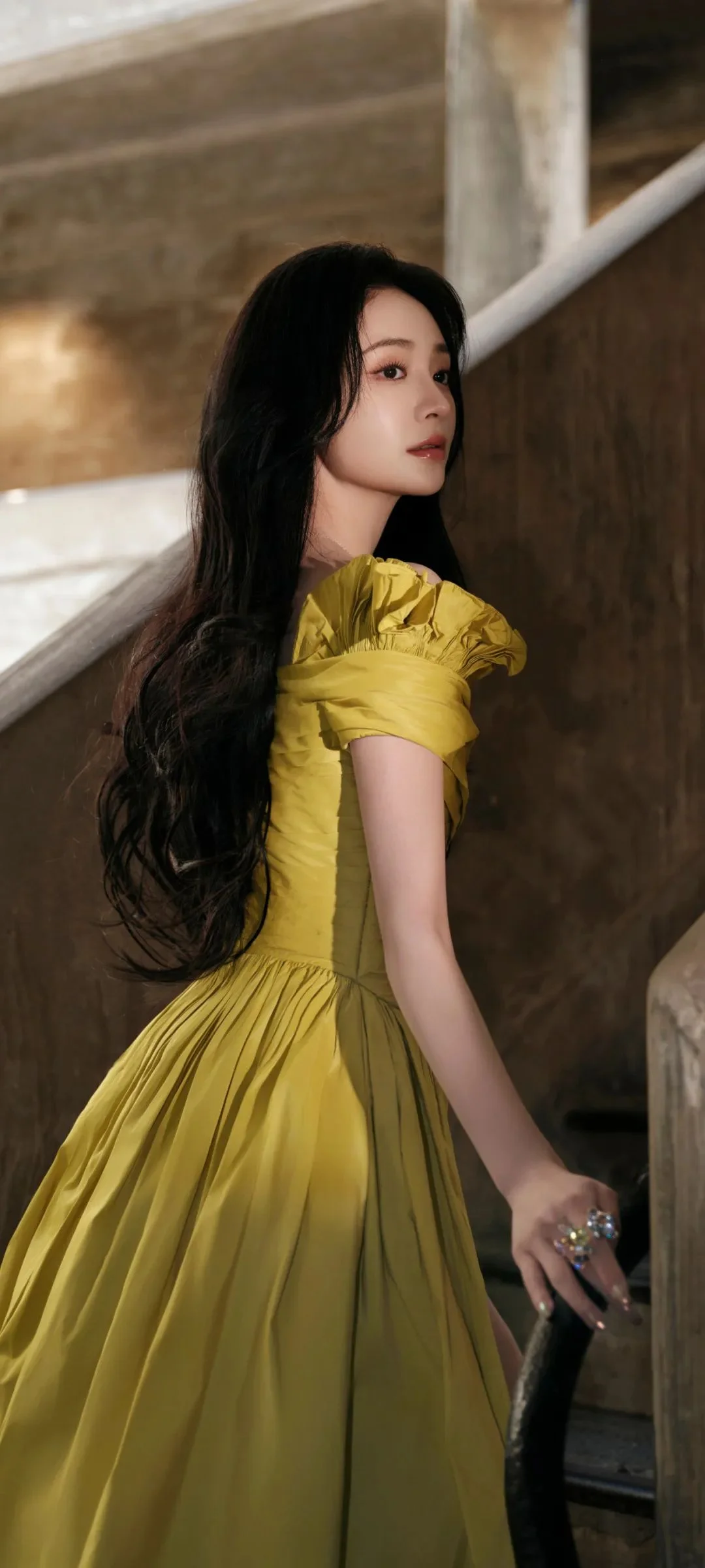 一名女子穿着黄色连衣裙站在室内楼梯旁。