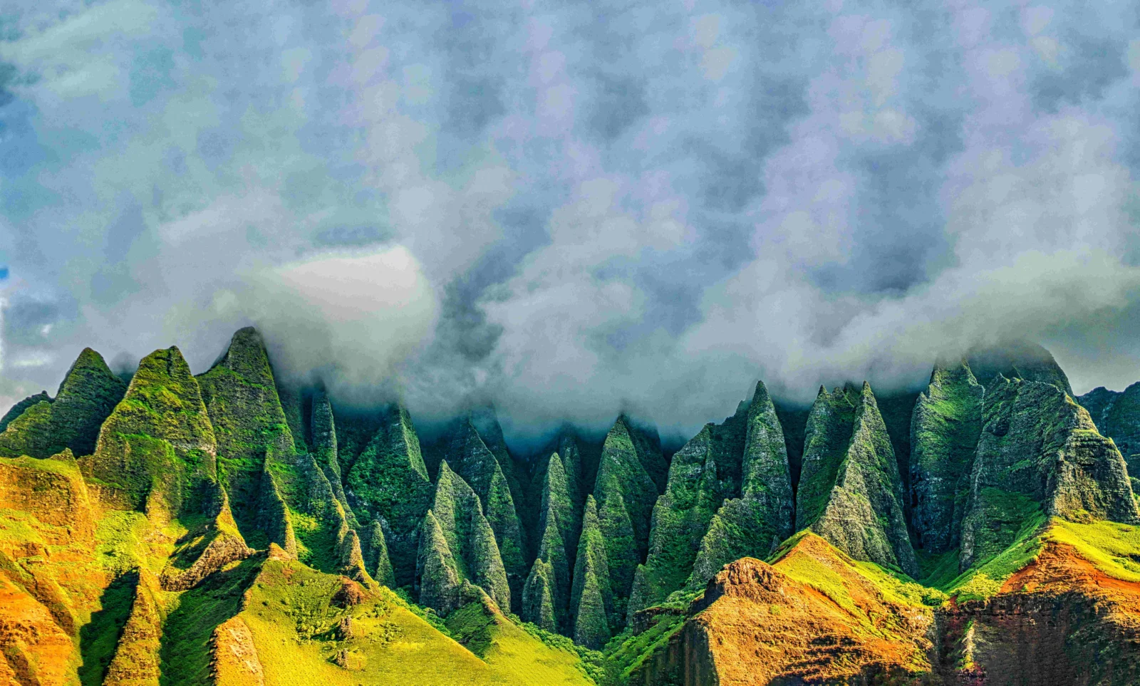 葱郁的尖峭山峰延伸在画面中，山顶被厚重云雾笼罩，前景沐浴在金色阳光下。