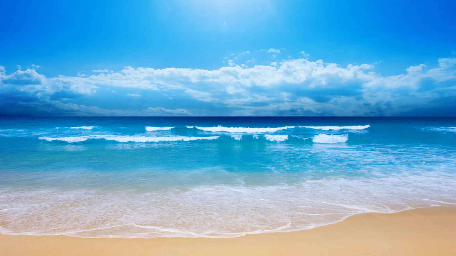蓝色天空下，海浪涌向沙滩，构成宁静的海岸景色。