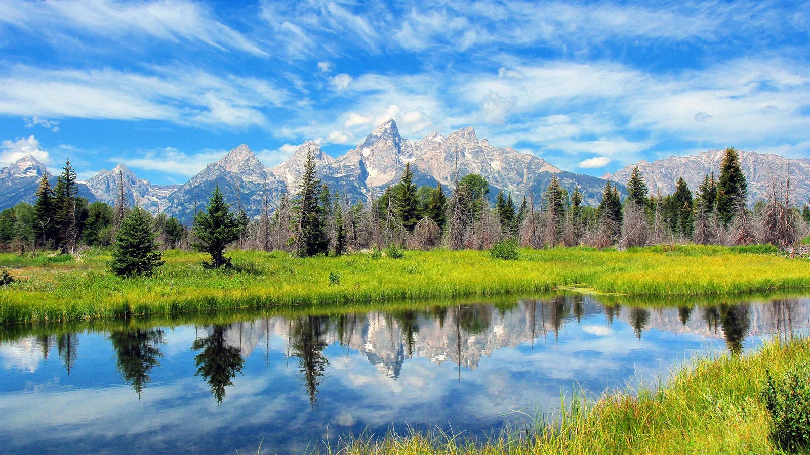 蓝天白云下的群山、森林与湖泊倒影构成宁静的自然风景。