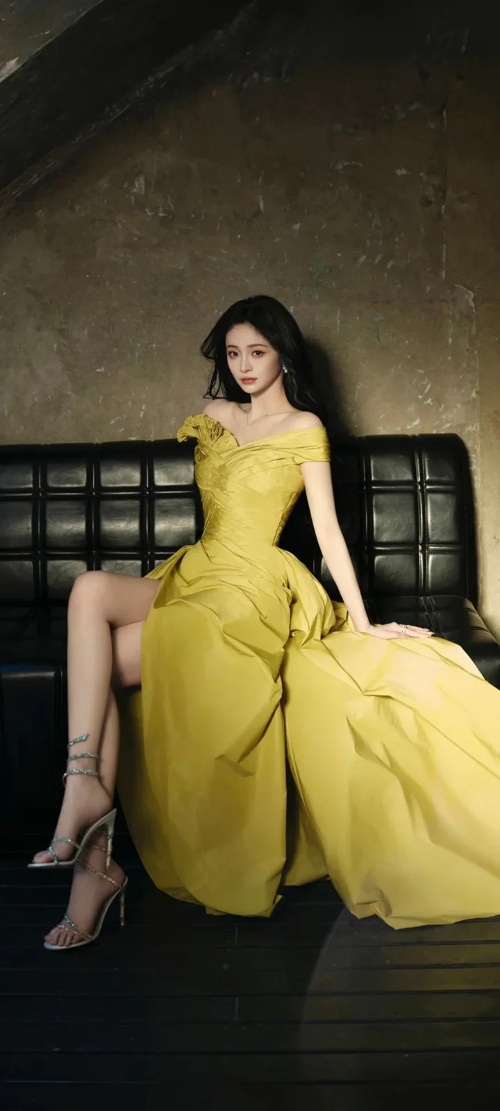 一名穿黄色礼服的女性坐在黑色沙发上。