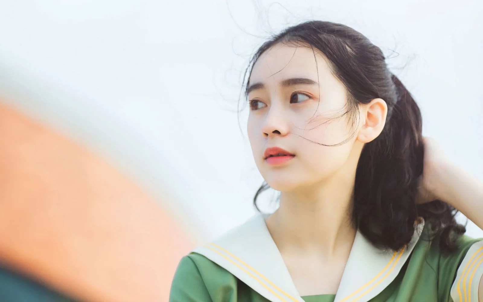 一名身穿绿色服装的女性在浅色背景前侧身望向一侧。