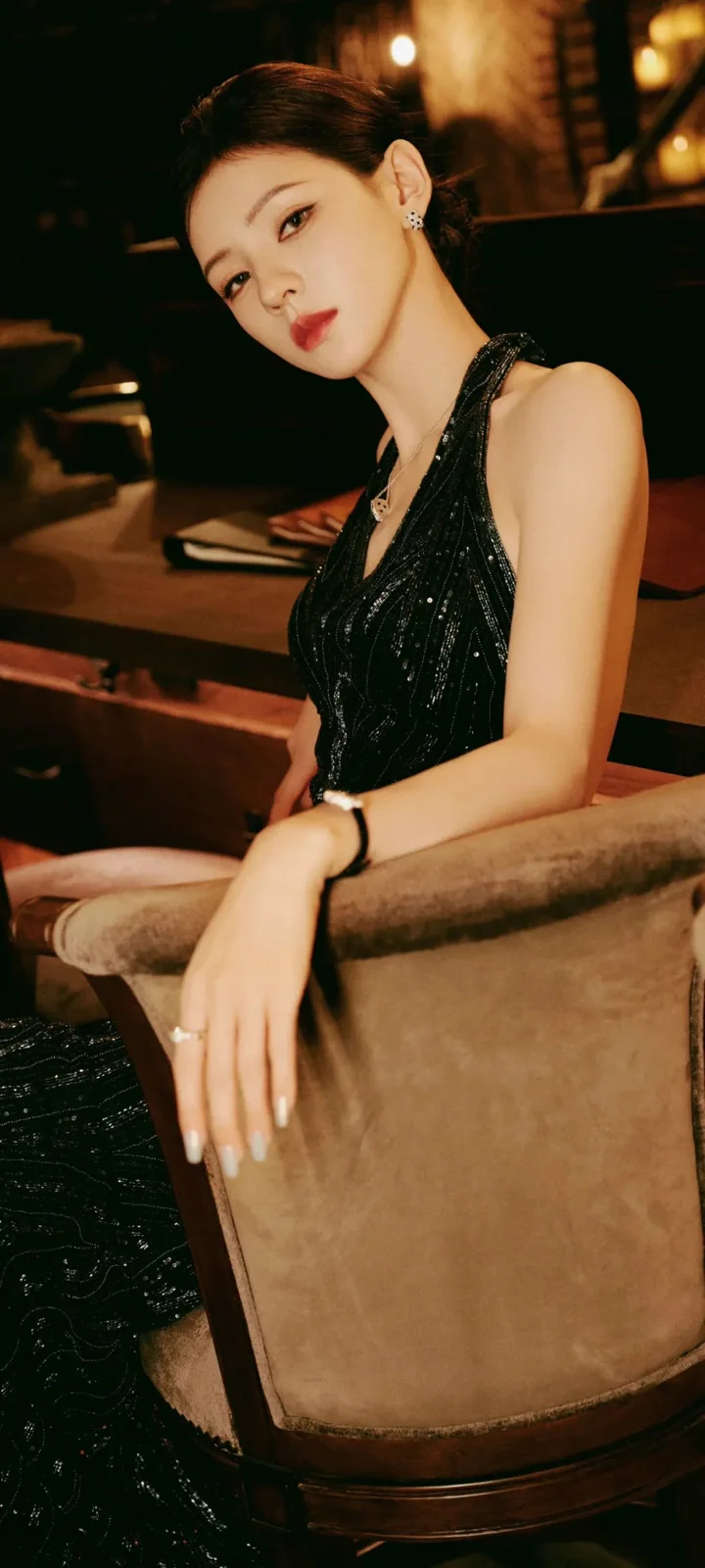一位成年女性身穿黑色无袖礼服坐在室内椅子上。